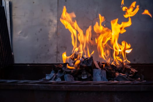 The firewood in the grill burns with a bright orange flame. Preparation for cooking meat on the grill in nature. Fire flames and smoke