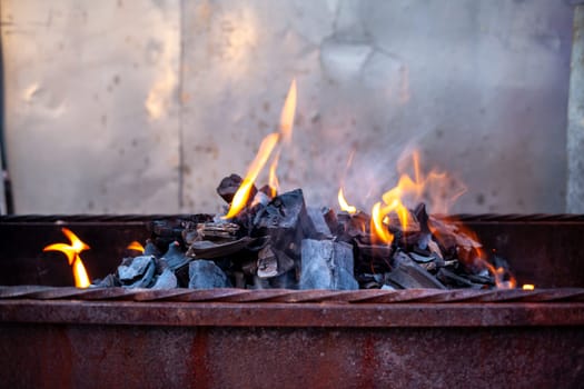 The firewood in the grill burns with a bright orange flame. Preparation for cooking meat on the grill in nature. Fire flames and smoke