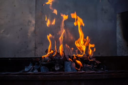 The firewood in the grill burns with a bright orange flame. Preparation for cooking meat on the grill in nature. Fire flames and smoke