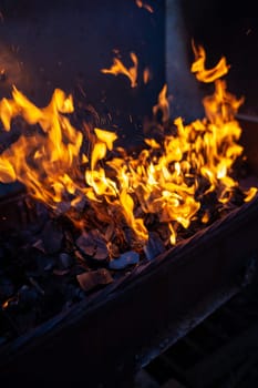 The firewood in the grill burns with a bright orange flame. Preparation for cooking meat on the grill in nature. Fire flames and smoke