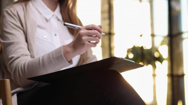 Serious woman fills out a questionnaire while sitting on a chair in the office