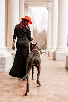 A photo of a woman and her Great Dane walking through a town, taking in the sights and sounds of the urban environment.