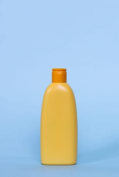 Yellow plastic cosmetic bottle on blue background. Kids hair shampoo, body lotion or sunscreen cream. Vertical, copy space