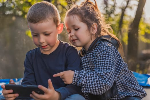 portrait of children who sit on a trampoline and look at the phone
