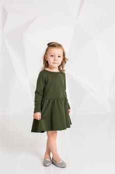 Beautiful little fashion model on white studio background. Portrait of cute girl posing in studio. Little blonde in dark green dress