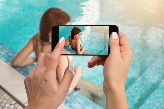 Closely image of female hands holding mobile phone with photo camera mode on the screen. Cropped image of beautiful long hair female model posing by the pool in wellness spa hotel resort.