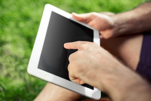 Young hipster boy sitting in the park and using modern digital tablet, male blogger using tablet pc outside, social networking concept