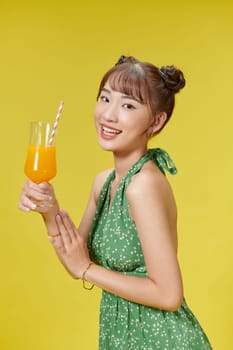A lovely asian woman in green summer dress, drinking orange juice