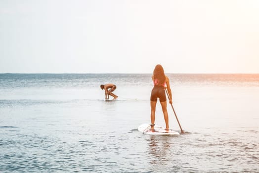 Sea woman and man on sup. Silhouette of happy young woman and man, surfing on SUP board, confident paddling through water surface. Idyllic sunset. Active lifestyle at sea or river