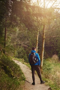 A guy tourist with a backpack stands on a mountain trail and looks into the distance. The concept of travel and adventure. Traveler Man with backpack mountaineering Travel Lifestyle concept mountains on background Summer trip vacations outdoor. Concept of travel and healthy, active lifestyle. Young guy with dreadlocks went hiking in mountains. Man with yellow backpack stands on top of hill and enjoys views of nature.