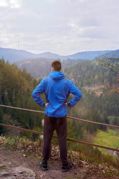 A guy tourist with a backpack stands on a mountain trail and looks into the distance. The concept of travel and adventure. Traveler Man with backpack mountaineering Travel Lifestyle concept mountains on background Summer trip vacations outdoor. Concept of travel and healthy, active lifestyle. Young guy with dreadlocks went hiking in mountains. Man with yellow backpack stands on top of hill and enjoys views of nature.