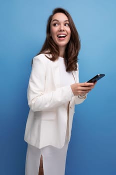 a woman with dark long hair in an elegant white dress holds a smartphone and chats on the Internet.