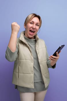 joyful blond 30 year old woman in casual clothes holds a mobile phone in her hands.