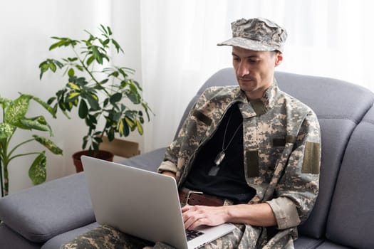 partial view of army soldier using laptop on couch.