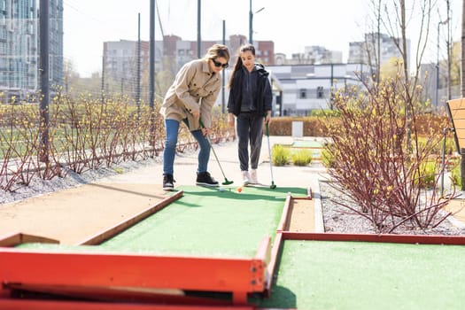 mother and daughter enjoying together playing mini golf in the city