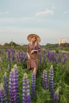 A beautiful woman in a straw hat walks in a field with purple flowers. A walk in nature in the lupin field.