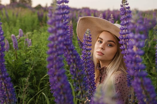 A beautiful woman in a straw hat walks in a field with purple flowers. A walk in nature in the lupin field.
