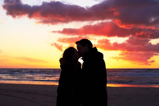 Beach, sunset and couple silhouette kiss in nature with love, freedom and romance outdoors. Shadow, romantic and people kissing at sunrise, sweet and together for travel, vacation or holiday in Bali.