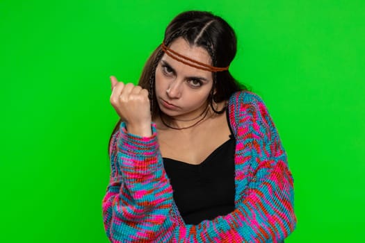 Aggressive angry young woman trying to fight at camera, shaking fist, boxing with expression, punishment, quarrel. Displeased attractive hippie girl isolated on chroma key background, green screen