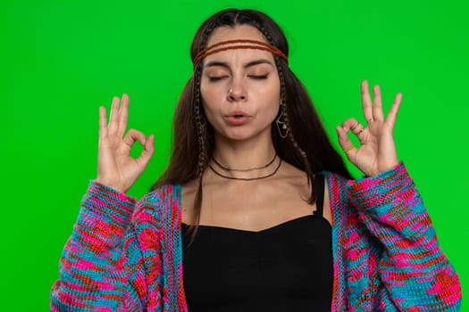 Keep calm down, relax, inner balance. Young woman breathes deeply with mudra gesture, eyes closed, meditating with concentrated thoughts, peaceful mind. Girl isolated on green chroma key background