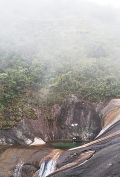 Beautifully carved colorful pools in the rock, surrounded by mist and jungle, with a flowing river in the background.