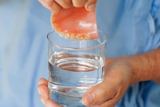 Asian senior woman patient clean teeth denture in a glass with solution for chew food.