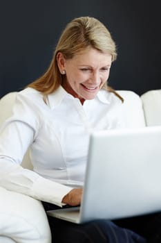 Time to do a little catching up. a smiling mature woman sitting on a couch and using a laptop