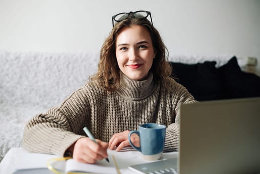 Home office of a young female English tutor with laptop, coffee, and notes, preparing for online lesson with student, sitting at kitchen table. Educator working remotely from home