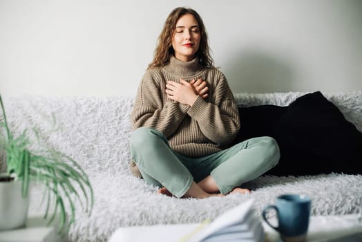Beautiful young woman in lotus pose on bed practicing pranayama breathing techniques, finding inner balance after a stressful day.