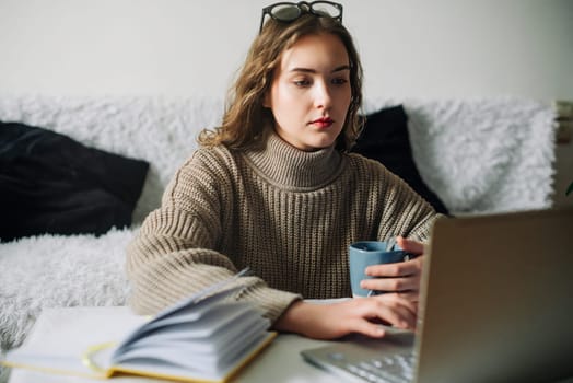 Portrait of a young teacher taking a break from work at her desk, checking email and sipping coffee, preparing lessons for students, relaxing between classes, education concept.