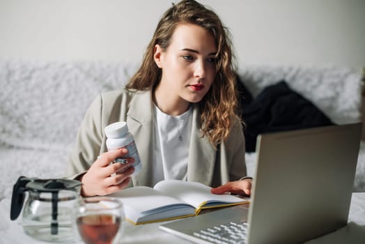 Healthy living and nutrition concept: young mom orders organic food supplements online, surrounded by bottles of vitamins, sitting at kitchen table with notebook and plastic jar of omega 3 fatty acids