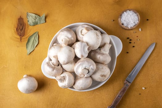 Close-up of champignon mushrooms on a white ceramic plate on a yellow background. Selective focus.