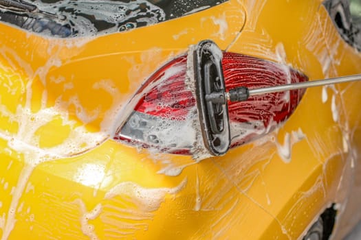 Yellow car rear light washed in self serve carwash. Brush cleaning shampoo covered red glass.