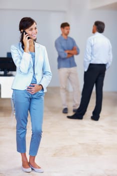 Business woman on call. Full length of young business woman talking on cellphone with staff in background