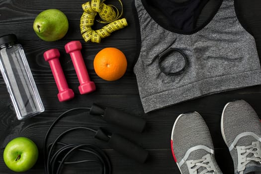 Athlete's set with female clothing, sneakers and bottle of water on dark background. Top view. Copy space. Still life. Ideal for sporty blog.