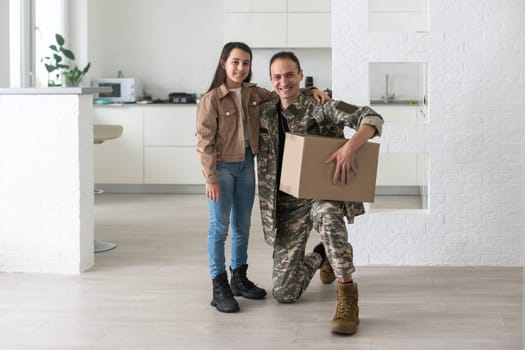 Military parents with daughter hugging, near cardboard boxes.