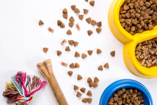 dry pet food in bowl and toys for dogs on white background top view. Still life. Copy space