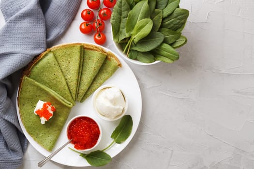 Spinach pancakes on a plate with soft cheese, caviar and cherry tomatoes on a gray background with textile. copy space