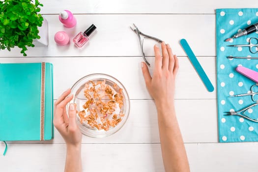 Beautiful woman's hands with perfect manicure in bowl of water on wooden background. Top view. Copy space. Nail Care.