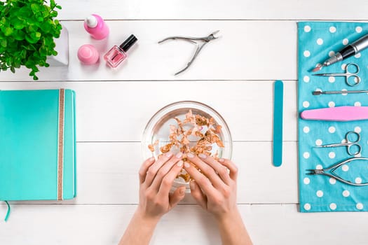 Beautiful woman's hands with perfect manicure in bowl of water on wooden background. Top view. Copy space. Nail Care.