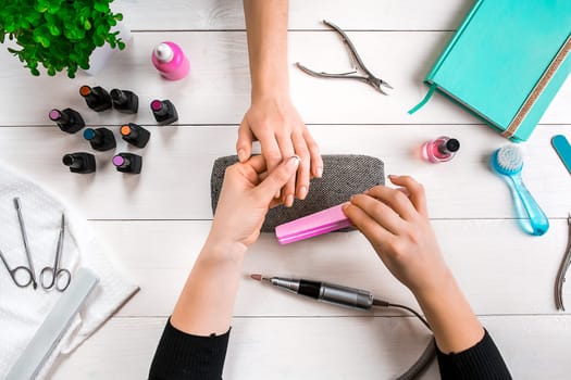 Closeup shot of a woman in a nail salon receiving a manicure by a beautician with nail file. Woman getting nail manicure. Beautician file nails to a customer.