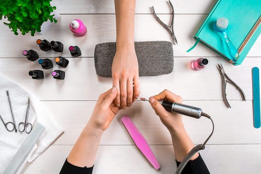Manicure for the client. Close-up of the hands of a manicurist and client on a wooden background. Nail care. Manicure set and nail polish.