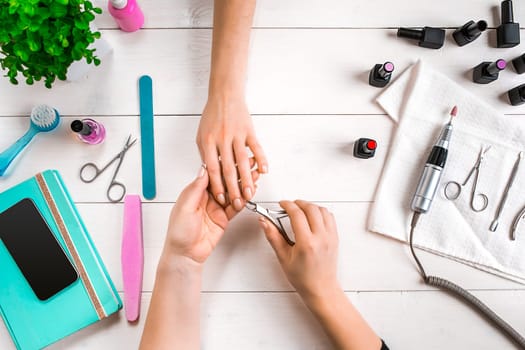 Manicure for the client. Close-up of the hands of a manicurist and client on a wooden background. Nail care. Manicure set and nail polish.