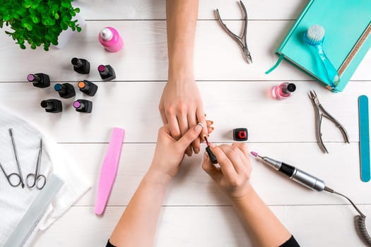 Nail care. Closeup of female hands filing nails with professional nail file in beauty nail salon. Close-up of beautician hands doing perfect manicure on woman's hands. Nail hygiene. Top view