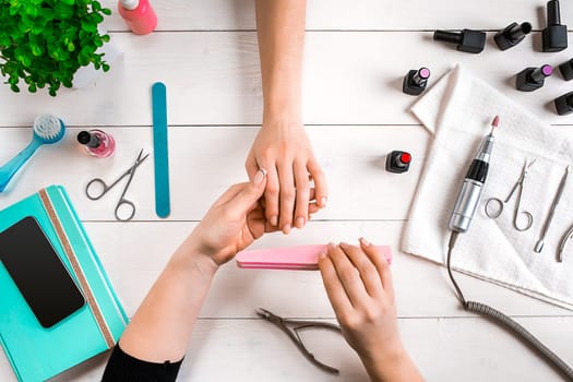 Manicure for the client. Close-up of the hands of a manicurist and client on a wooden background. Nail care. Manicure set and nail polish.