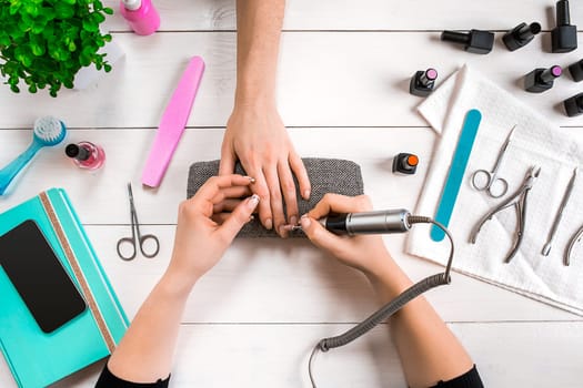 Closeup shot of a woman in a nail salon receiving a manicure by a beautician with nail file. Woman getting nail manicure. Beautician file nails to a customer.