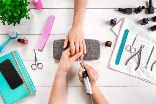 Closeup shot of a woman in a nail salon receiving a manicure by a beautician with nail file. Woman getting nail manicure. Beautician file nails to a customer.