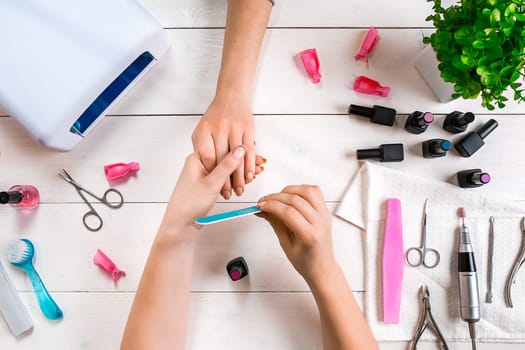 Manicure for the client. Close-up of the hands of a manicurist and client on a wooden background. Nail care. Manicure set and nail polish.