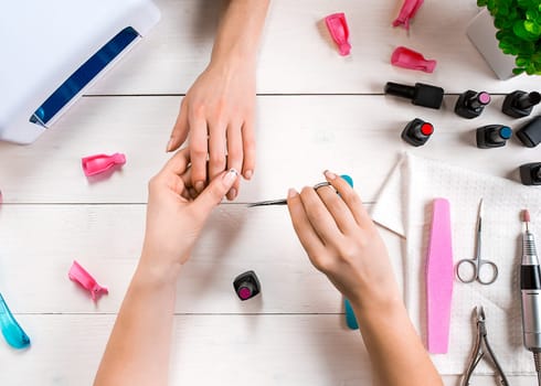 Manicure for the client. Close-up of the hands of a manicurist and client on a wooden background. Nail care. Manicure set and nail polish.