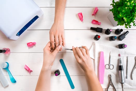 Nail care. Closeup of female hands filing nails with professional nail file in beauty nail salon. Close-up of beautician hands doing perfect manicure on woman's hands. Nail hygiene. Top view